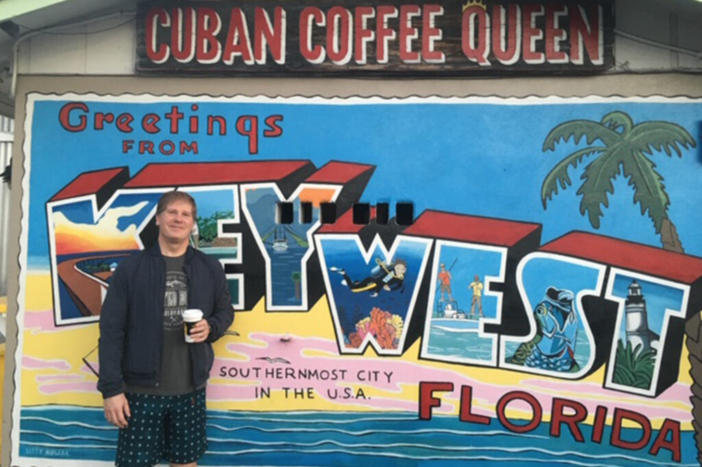 Peter Hinman standing in front of KeyWest postcard graphic and Cuban Coffee sign