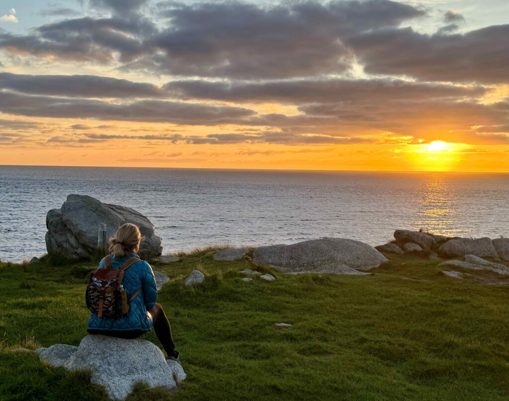 women with backpack looking out towards a ocean view at sunrise