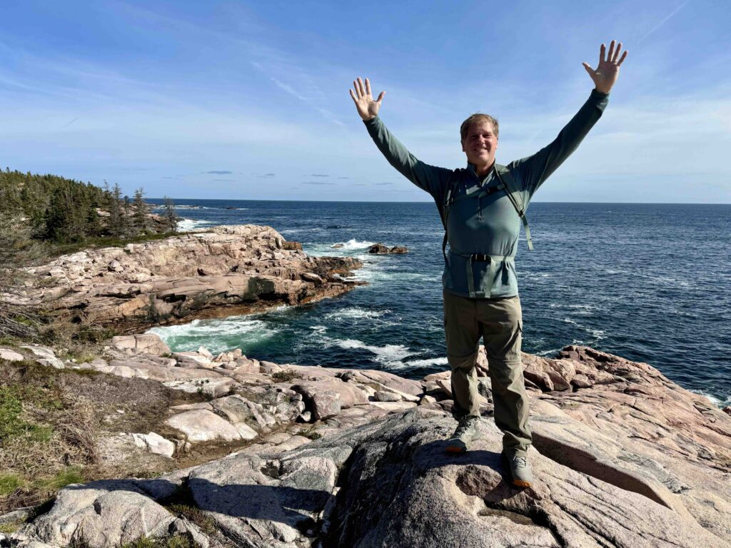 man standing on rocks with hands in the air on the coastal trails of Jack Pine Trail